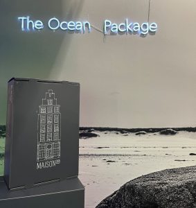 Mehrweg Versandbox vor einem Wandbild von einem Strand und dem The Ocean Packages Logo