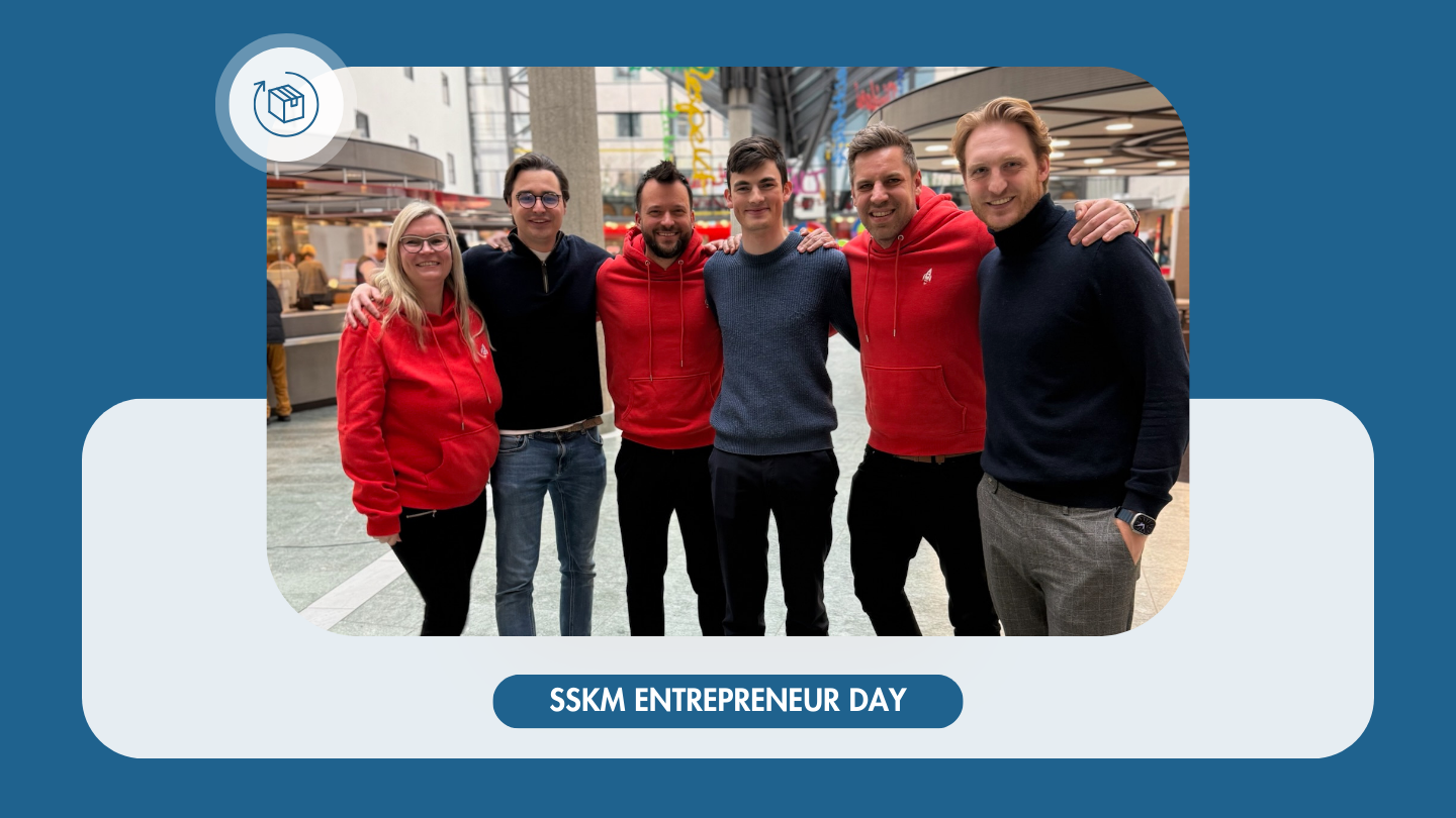 Eine Gruppe von sechs Personen posiert für ein Gruppenfoto auf dem SSKM Entrepreneur Day. Drei von ihnen tragen rote Hoodies mit einem Raketenlogo, während die anderen dunkel gekleidet sind. Der Hintergrund zeigt eine moderne Innenarchitektur mit Glasdach und bunten Elementen.