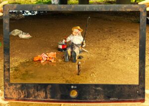 Trash Art Performance: Eine Puppenfigur in einem weggeworfenen Fernseher-Rahmen fischt Müll aus einer Pfütze, um auf die Verschmutzung aufmerksam zu machen.