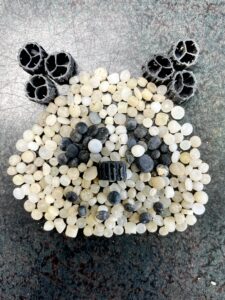 Panda-Gesicht, zusammengesetzt aus Tausenden von Nurdles (Plastikgranulat) und schwarzen Kunststoffteilen, um auf Mikroplastik-Verschmutzung aufmerksam zu machen.