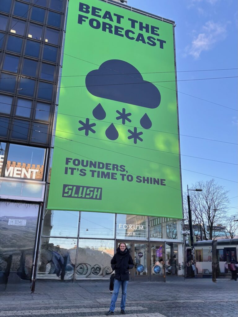 Gründer Joshua von The Ocean Package steht vor einem großen, grünen Plakat der SLUSH in Helsinki, dem Treffpunkt für Innovation in der Logistik.